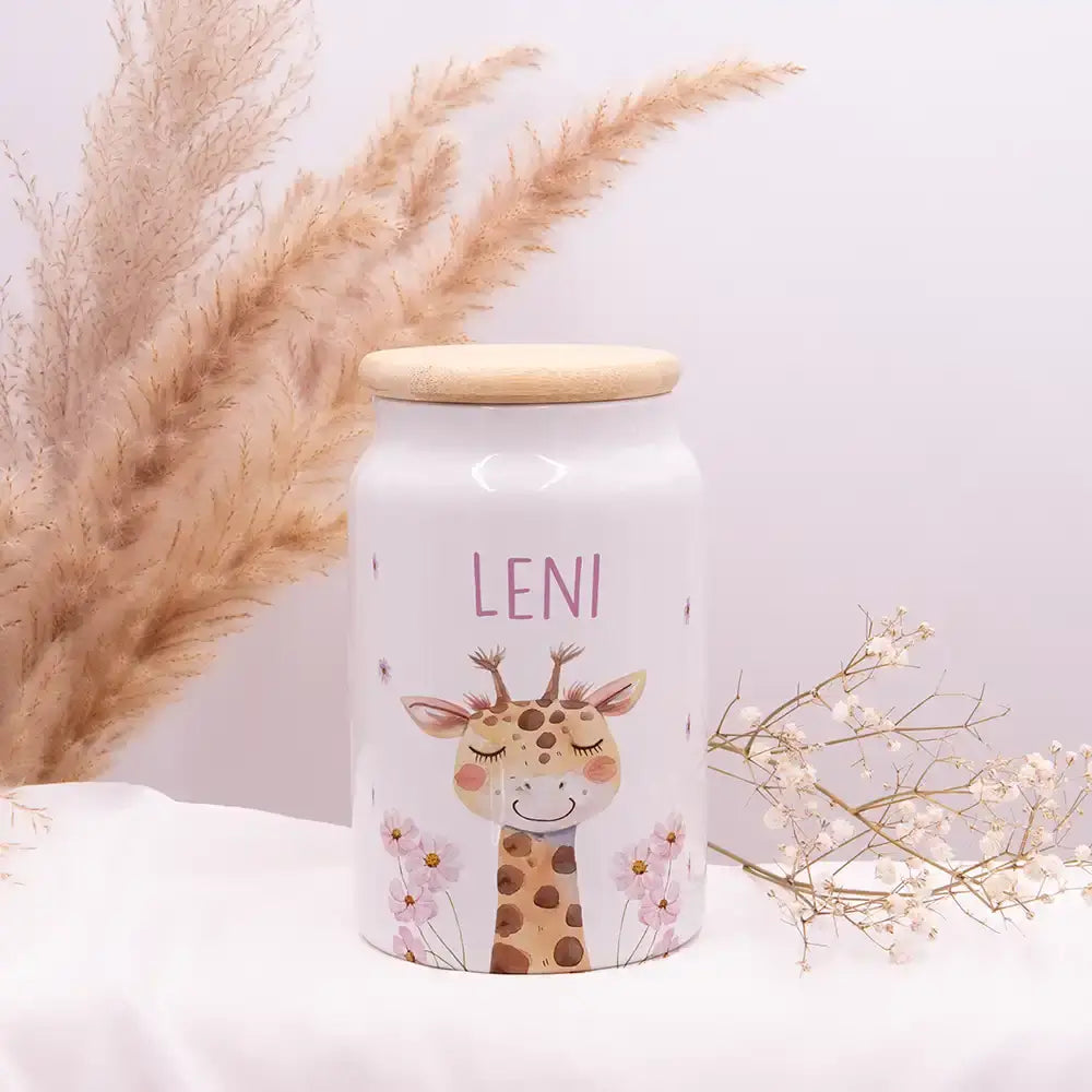 Personalisierbare Keksdose aus weißer Keramik mit Holzdeckel, graviert mit dem Namen "LENI" und niedlichem Giraffen-Motiv mit rosa Blumen, dekorativ arrangiert mit Pampasgras