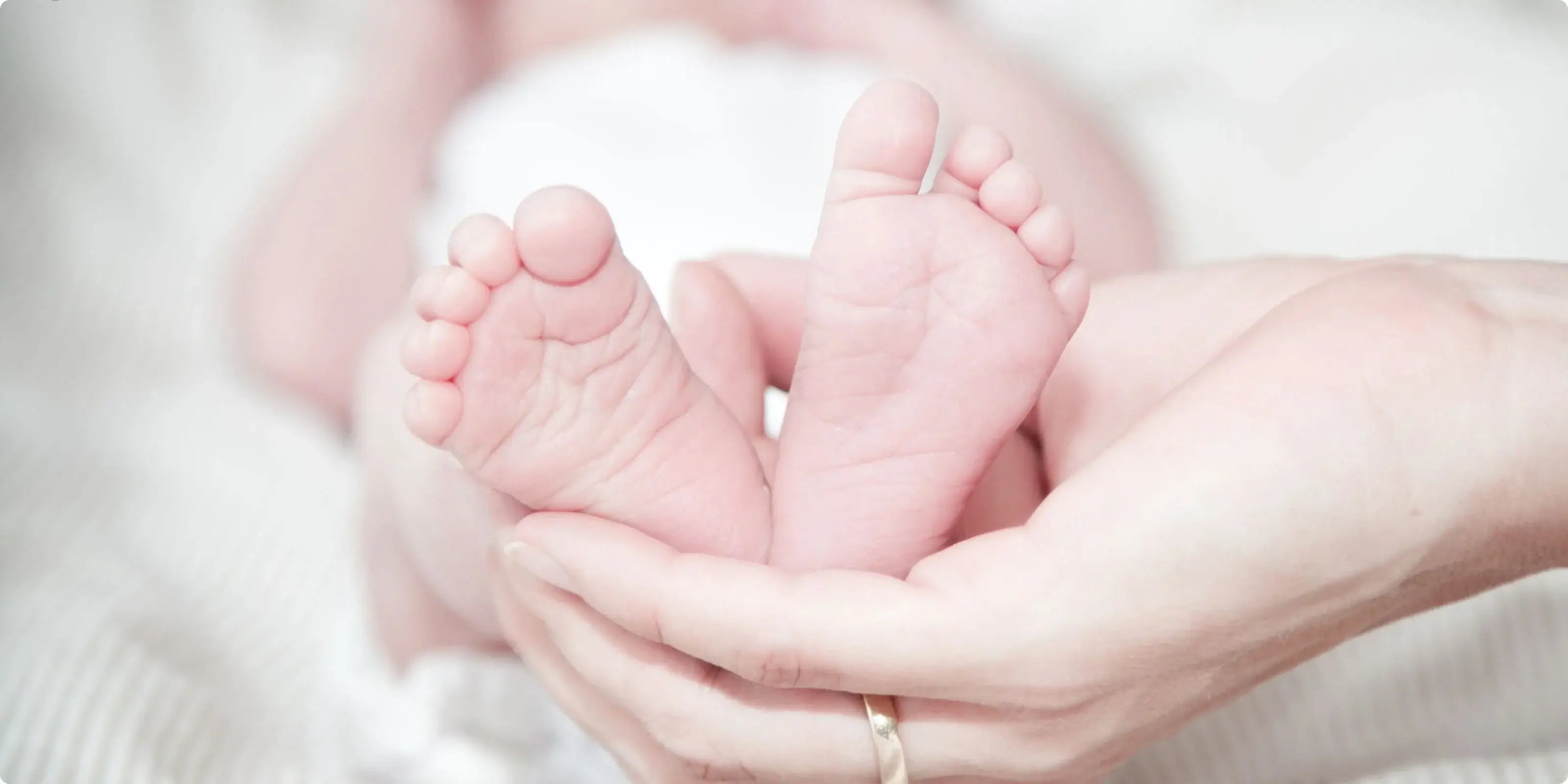 Zarte Babyfüße in liebevollen Händen gehalten - Nahaufnahme von Neugeborenen-Füßchen auf weicher weißer Unterlage als Symbol für Glückwünsche zur Geburt und elterliche Zuneigung