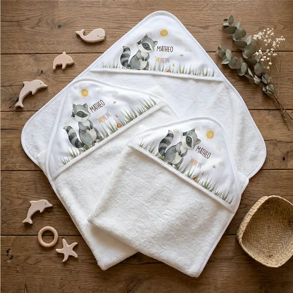 Personalisiertes Kapuzenhandtuch Baby Waschbär Wiese – Flatlay mit Eukalyptus und Beißring